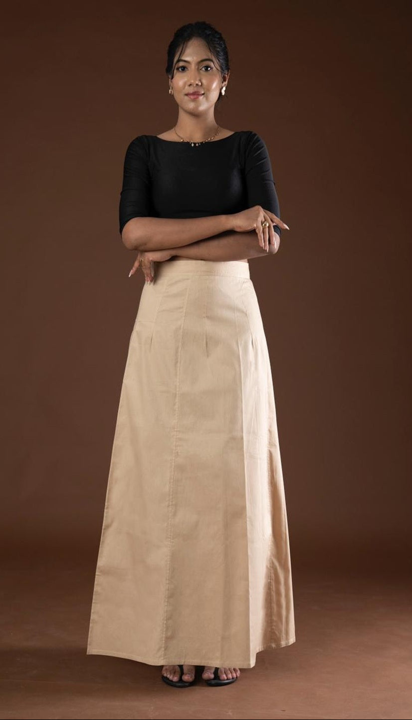 Woman wearing a black top and beige petticoat inskirt against a brown background