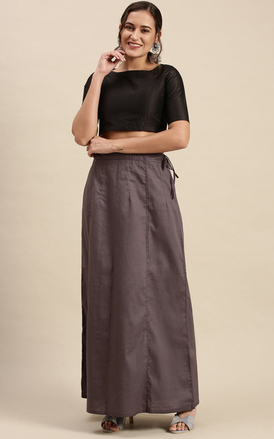 Woman wearing a black top and gray petticoat inskirt on a beige background