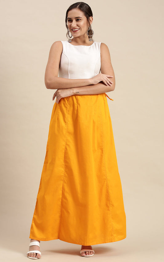 Woman wearing a white sleeveless top and amber orange petticoat inskirt on a beige background