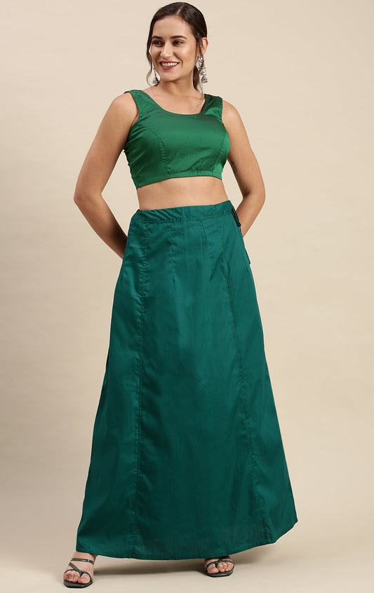 Woman wearing a green outfit with a top and petticoat inskirt on a beige background