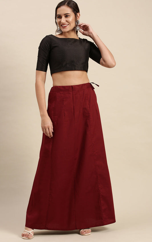 Woman wearing a black top and maroon petticoat inskirt on a beige background