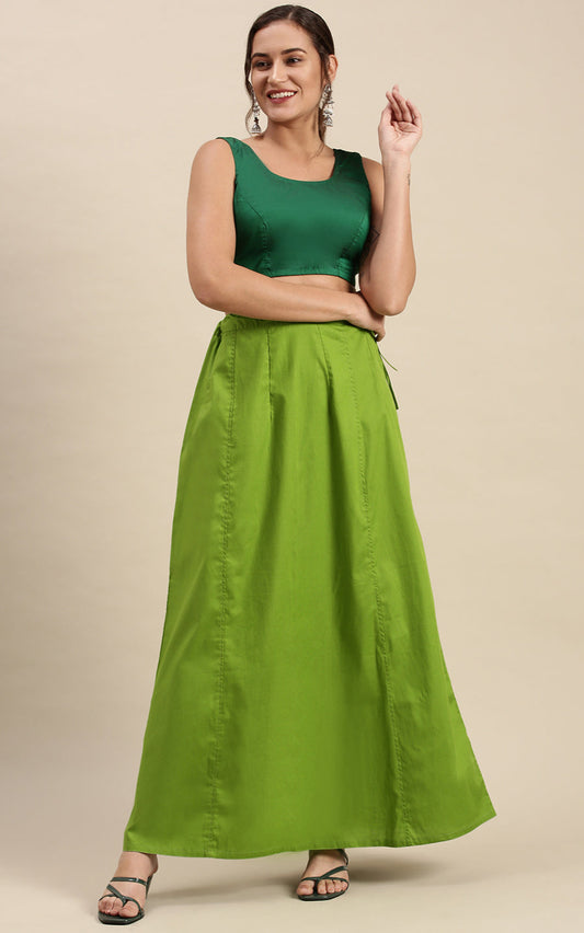 Woman wearing a green sleeveless top and petticoat inskirt against a beige background
