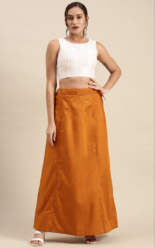 Woman wearing a white sleeveless top and mustard skirt on a beige background